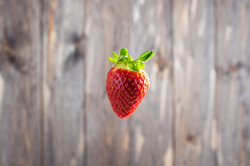 One strawberry is hanging in the air. Background with the text of an old wooden table top.