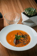 Gourmet serving of spicy tomato soup with fried mussels and chili peppers on a plate and wooden table isolated. Delicious seafood mussels . Lemon and baguette . Clams in the shells. Top view.