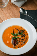 Gourmet serving of spicy tomato soup with fried mussels and chili peppers on a plate and wooden table isolated. Delicious seafood mussels . Lemon and baguette . Clams in the shells. Top view.