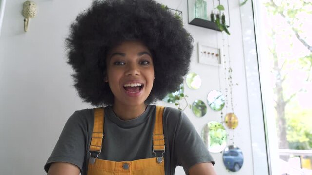 Young happy African American mixed race hipster vlogger woman waving hand looking at webcam talking to camera sit at table video conference calling in virtual chat meeting with social distance friend.
