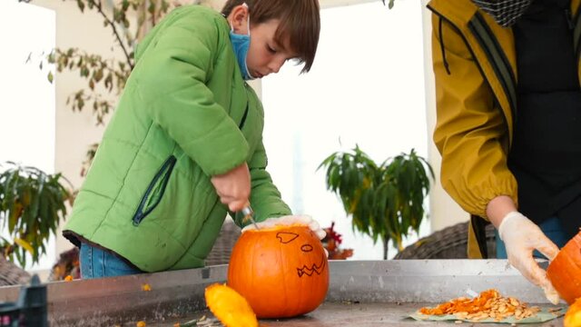 A teacher with students on the terrace of an elementary school gives a master class in decor carving a pumpkins for Halloween. Pumpkin carving safety tips to prevent hand injuries of pupil.