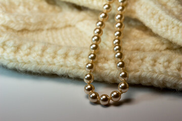 Macro abstract full frame background of cream color woolen mittens texture, adorned with a string of pearls