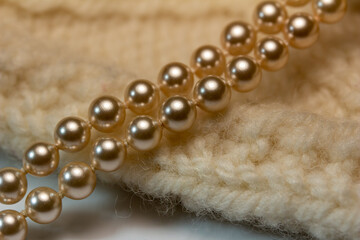 Macro abstract full frame background of cream color woolen mittens texture, adorned with a string of pearls