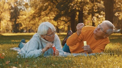 Romance at old age. Elderly couple blowing soap bubbles in the park in autumn. High quality photo