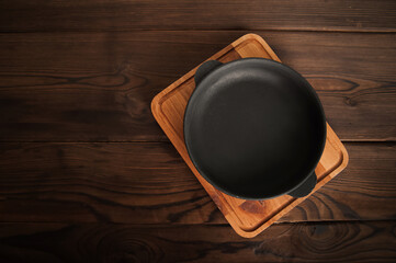 Empty cast iron round frying pan on textured wooden background close-up and copy space.