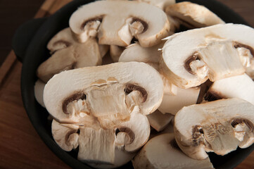 Mushrooms in a black plate on a wooden board. Chopped champignons in a cast iron skillet close-up...