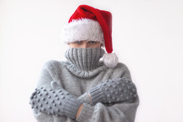 A teenage girl in a grey knitted sweater, mittens and a red Santa hat pulled the collar of the sweater over her face and hugged herself. She was cold. The concept of Christmas, New year and winter