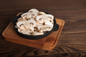 Mushrooms in a black plate on a wooden board. Chopped champignons in a cast iron skillet close-up and copy space.