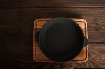 Empty cast iron round frying pan on textured wooden background close-up and copy space.