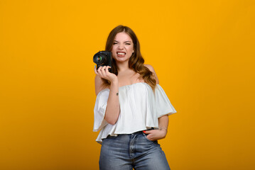 Young female photographer with camera over yellow background