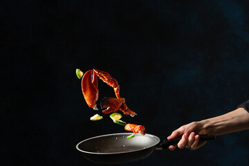Close-up view of the professional chef tossed crab lags with lime in frying pan on black background. Backstage of cooking delicious meal for dinner. Seafood concept. Frozen motion. Asian recipe. © Anton
