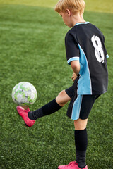 young caucasian kid boy with soccer ball is in motion on green grass background, boy in uniform is in action, run and play with ball