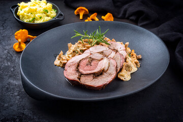 Traditioneller französischer gegrillter Lammbraten  aufgeschnitten mit Pfifferlingen in Rahmsauce und Kartoffel Püree angeboten als close-up auf einem gusseisernen design Teller