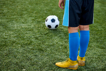 Obraz premium kid boy kicking soccer ball on sports field, cropped child boy in uniform and sneakers play football in stadium