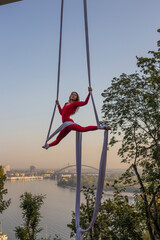 beautiful and professional Aerial silk artist practicing in the red suit under the famous glass bridge over the Kiev city