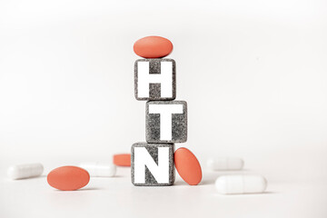 a group of white and red pills and cubes with the word HTN Hypertension. on them, white background. Concept carehealth, treatment, therapy.