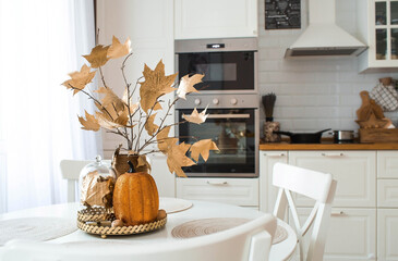 Branches with Golden leaves and a pumpkin on a tray. In the background-the interior of a white...