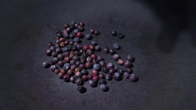 Close up of human hand putting dried juniper berries into dark grey cast iron pan for roasting