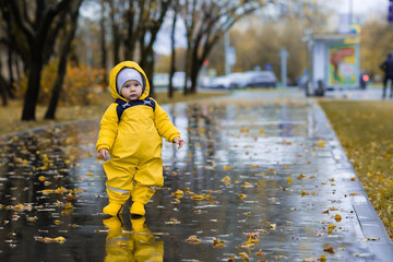 Cute little boy on a wet road. Happy child walking in the rain. The kid wears a fashionable yellow...