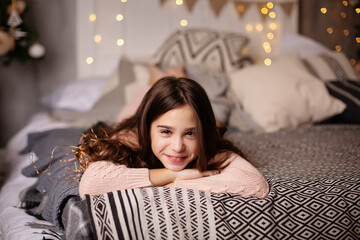 Beautiful little dark-haired girl in the studio with New Year's decor and confetti. The child is having fun and playing. Portrait of a child. The child lying on the bed near the Christmas tree