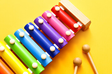 Rainbow colored toy xylophone with two sticks on yellow background. Close up