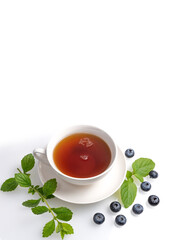 A Cup of black tea on a saucer with mint leaves and blueberries on a white isolated background. Copy space