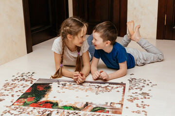 Girl and boy collect puzzle on the floor in the house. Sister and brother playing together