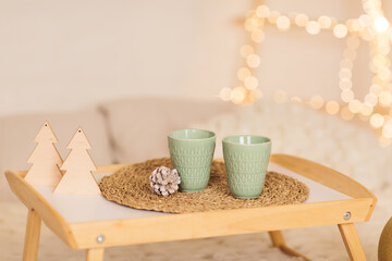 Home interior. A bed with a white knitted blanket. Breakfast table-tray with two cups on the bed. Elements of the Christmas holiday. Close-up
