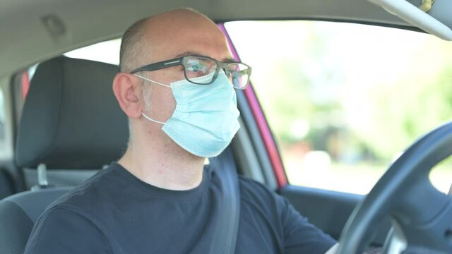 Escaping home life, driving to new destinations. In the covid era, a Caucasian man with a mask to defend himself from the coronavirus drives his car to new destinations: he is focused on driving.