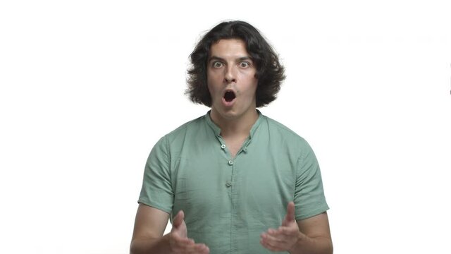 Video of handsome hispanic guy in green shirt, drop jaw and gasping amazed, looking impressed and fascinated with something, standing over white background