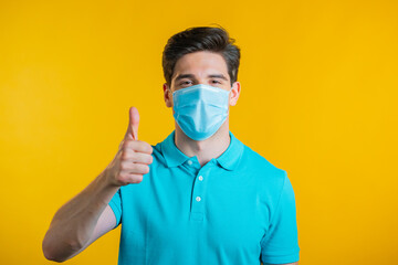 Handsome man shows thumbs up, Like gesture. Happy guy on yellow background. Winner. Success. Positive male model smiles to camera. Body language. Covid-19, coronavirus concept.