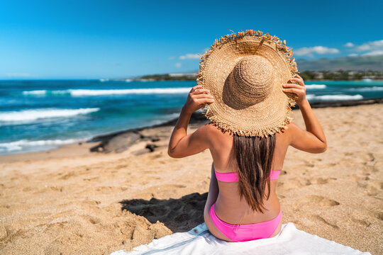Beach girl in pink bikini wearing floppy hat sun tanning on Beach holiday in Caribbean destination sunbathing relaxing with view on ocean.