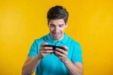 Handsome man playing game on smartphone on yellow studio wall. Using modern technology - apps, social networks.