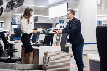 Business trip. Handsome young businessman in suit holding his passport and talking to woman at airline check in counter in the airport - 386523265