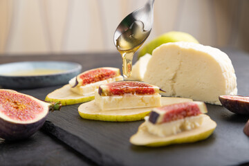Summer appetizer with pear, cottage cheese, figs and honey on a black concrete background. Side view, selective focus.