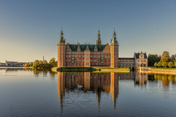 Frederiksborg castle glimmers in the sunshine and is reflected in the mirror-shiny lake
