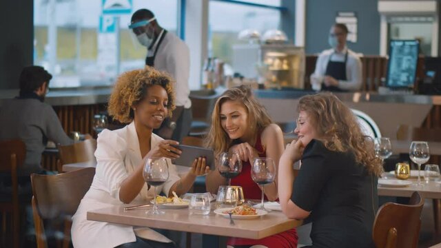 Diverse beautiful female friends in restaurant using tablet computer
