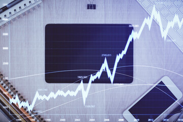 Double exposure of forex graph hologram over desktop with phone. Top view. Mobile trade platform concept.