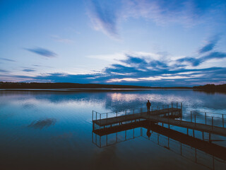 Sunset over a river with pier and a forest on horizon. Almost dusk.