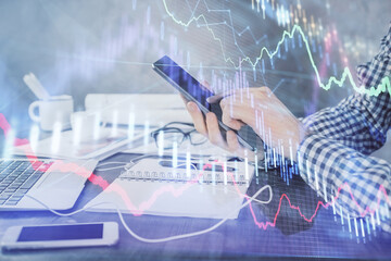 Double exposure of man's hands holding and using a digital device and forex graph drawing. Financial market concept.