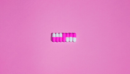 White and pink pills on a road on pink background. Medicine concept. Flat lay. Copy space.