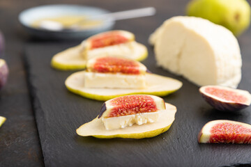 Summer appetizer with pear, cottage cheese, figs and honey on a black concrete background. Side view, selective focus.