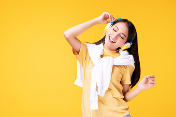 Cheerful enjoy young woman wearing headphones listening to music form smartphone and dancing relax over isolated yellow background. Lifestyle leisure with hobby concept.
