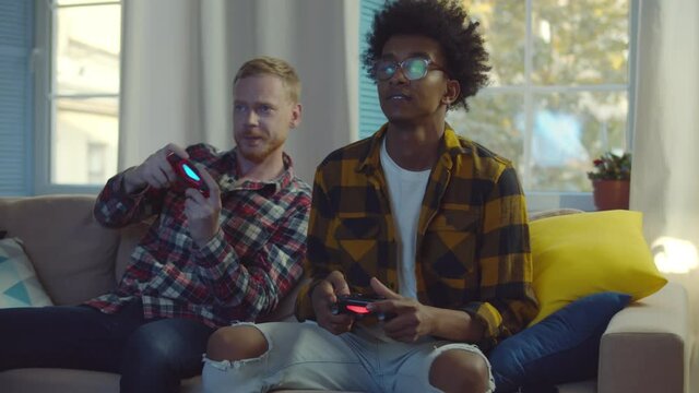 Smiling diverse male friends with gamepads playing video game at home