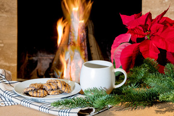 a cup of coffee and a plate of cookies by a fireplace with a poinsettia for Christmas