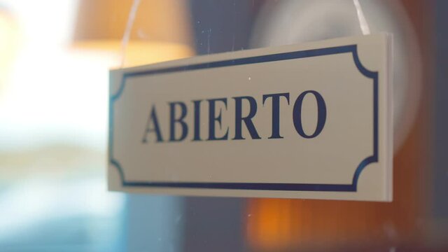 Close up of human turning abierto cerrado sign hanging on glass door of cafe