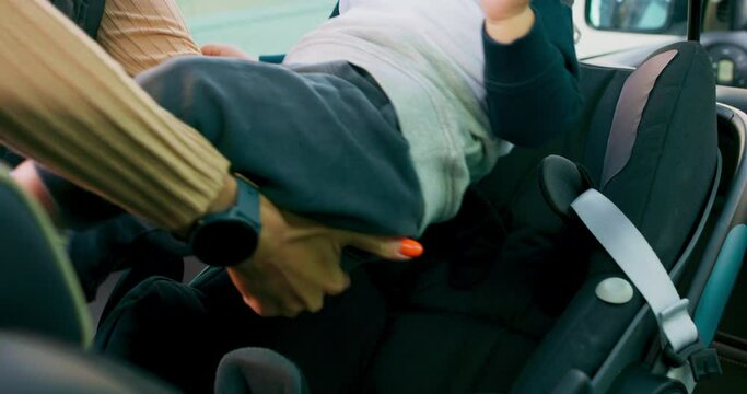 Camera inside the car. Closeup baby car seat. boy appears, carried on hands of his mother, who puts the baby inside the baby car seat. Baby is crying, mother fastens seat belts. Slow motion