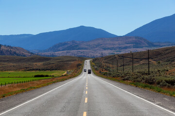View of Scenic Road surrounded by Farmland and Mountains on a Sunny Summer Day in Canadian Nature. Taken on the Trans-Canada Highway, West of Kamloops, British Columbia, Canada.