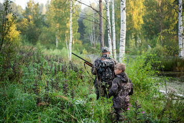 Father's day. Father with gun showing something to son while hunting on a nature. Happy family,...