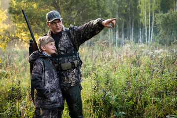 Father's day. Father with gun showing something to son while hunting on a nature. Happy family,...